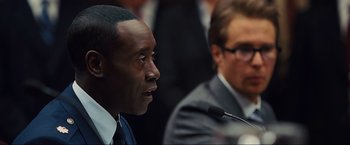 Movie still from “Iron Man 2” (2010), directed by Jon Favreau – A man in a suit and tie speaking at a microphone; Close Up shot, Over the shoulder angle