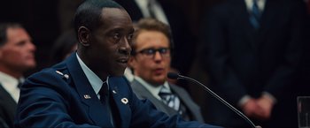 Movie still from “Iron Man 2” (2010), directed by Jon Favreau – A man in a suit is speaking at a microphone; Close Up shot, Over the shoulder angle