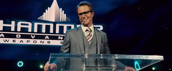 Movie still from “Iron Man 2” (2010), directed by Jon Favreau – A man in a suit and tie standing at a podium; Medium shot, Low angle