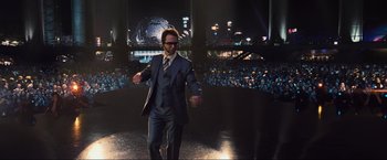 Movie still from “Iron Man 2” (2010), directed by Jon Favreau – A man in a suit and tie standing in front of an audience; Wide shot, High angle