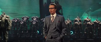 Movie still from “Iron Man 2” (2010), directed by Jon Favreau – A man in a suit and tie standing in front of a group of robots; Medium shot, Low angle