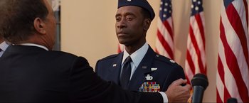 Movie still from “Iron Man 2” (2010), directed by Jon Favreau – A man in a military uniform standing in front of two american flags; Close Up shot, Over the shoulder angle