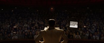 Movie still from “Isle of Dogs” (2018), directed by Wes Anderson – A man is standing in front of an audience; Extreme Wide shot, High angle