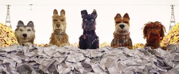 Movie still from “Isle of Dogs” (2018), directed by Wes Anderson – A group of dogs that are sitting in a pile of papers; Medium shot, High angle