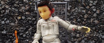 Movie still from “Isle of Dogs” (2018), directed by Wes Anderson – A doll is sitting on a chair in front of a pile of rocks; Close Up shot, High angle