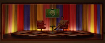 Movie still from “Isle of Dogs” (2018), directed by Wes Anderson – A man sitting on a chair in front of a painting; Wide shot, High angle