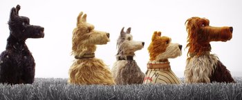 Movie still from “Isle of Dogs” (2018), directed by Wes Anderson – A group of dogs that are sitting in the grass; Medium shot, Low angle