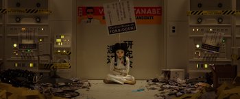 Movie still from “Isle of Dogs” (2018), directed by Wes Anderson – A woman sitting on the ground with a sign above her head; Wide shot, High angle