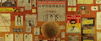 Movie still from “Isle of Dogs” (2018), directed by Wes Anderson – A person standing in front of a wall covered with papers; Medium shot, Overhead angle