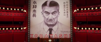 Movie still from “Isle of Dogs” (2018), directed by Wes Anderson – A large poster of a man in a suit and tie; Medium shot, Low angle