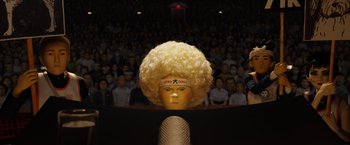 Movie still from “Isle of Dogs” (2018), directed by Wes Anderson – A crowd of people in a room with a gold head; Extreme Close Up shot, Low angle