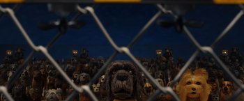 Movie still from “Isle of Dogs” (2018), directed by Wes Anderson – A dog behind a fence with a crowd of dogs behind it; Wide shot, High angle