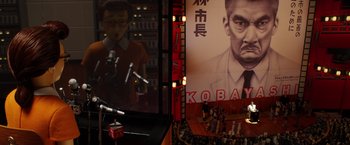 Movie still from “Isle of Dogs” (2018), directed by Wes Anderson – An audience is sitting in front of a large poster of a man; Extreme Wide shot, High angle