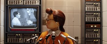 Movie still from “Isle of Dogs” (2018), directed by Wes Anderson – A person with a wig and headphones on in front of microphones and a television; Medium shot, Low angle