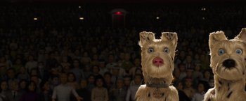 Movie still from “Isle of Dogs” (2018), directed by Wes Anderson – A crowd of people in a room with a dog costume; Close Up shot, High angle