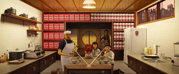 Movie still from “Isle of Dogs” (2018), directed by Wes Anderson – A group of people standing around a table with bowls; Wide shot, Low angle