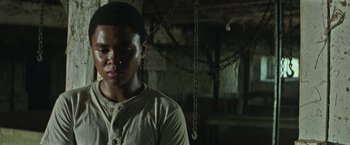 Movie still from “It” (2017), directed by Andy Muschietti – A young man standing in front of a chain link fence; Close Up shot, Low angle