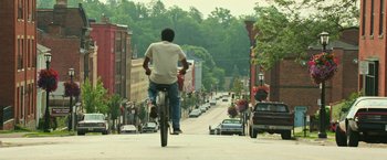 Movie still from “It” (2017), directed by Andy Muschietti – A man riding a bike down the middle of a street; Wide shot, High angle