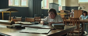 Movie still from “It” (2017), directed by Andy Muschietti – A person sitting at a table in a room; Medium shot, Low angle