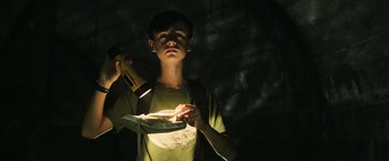 Movie still from “It” (2017), directed by Andy Muschietti – A young boy holding a flashlight and a plate of food; Medium shot, Low angle