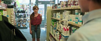 Movie still from “It” (2017), directed by Andy Muschietti – A woman standing in front of a shelf filled with many items; Medium shot, Over the shoulder angle
