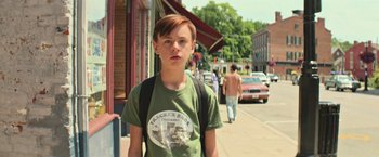 Movie still from “It” (2017), directed by Andy Muschietti – A young boy is standing on the sidewalk; Medium shot, Over the shoulder angle