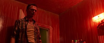 Movie still from “It” (2017), directed by Andy Muschietti – A man standing in front of a red wall in a room; Medium shot, Low angle