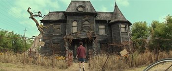 Movie still from “It” (2017), directed by Andy Muschietti – A man standing in front of an abandoned house; Wide shot, Low angle