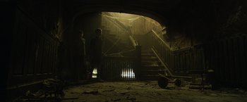 Movie still from “It” (2017), directed by Andy Muschietti – Two people standing in a dark room with stairs; Wide shot, Low angle