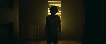 Movie still from “It” (2017), directed by Andy Muschietti – A person standing in a room with a light shining on them; Wide shot, Low angle