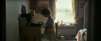 Movie still from “It” (2017), directed by Andy Muschietti – A woman sitting at a desk typing on a computer; Wide shot, High angle