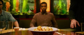 Movie still from “It Chapter Two” (2019), directed by Andy Muschietti – A man sitting in front of a bowl filled with food; Medium shot, Over the shoulder angle