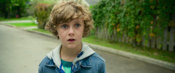 Movie still from “It Chapter Two” (2019), directed by Andy Muschietti – A young boy with blue eyes is standing on the street; Close Up shot, High angle