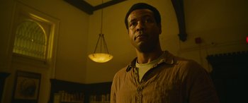 Movie still from “It Chapter Two” (2019), directed by Andy Muschietti – A man standing in a dimly - lit room with a light hanging from the ceiling; Close Up shot, Low angle