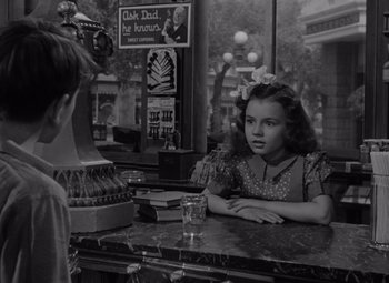 Movie still from “It's a Wonderful Life” (1946), directed by Frank Capra – A young girl sitting at a table in front of a glass of water; Medium shot, Over the shoulder angle
