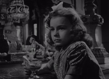 Movie still from “It's a Wonderful Life” (1946), directed by Frank Capra – A little girl sitting at a table holding a glass; Close Up shot, Low angle