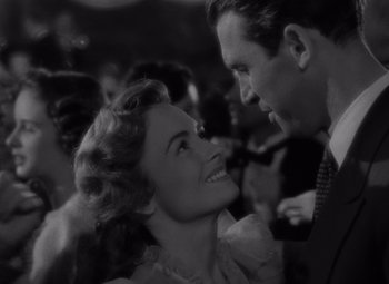 Movie still from “It's a Wonderful Life” (1946), directed by Frank Capra – A man and a woman smiling at each other in front of a crowd; Close Up shot, Over the shoulder angle