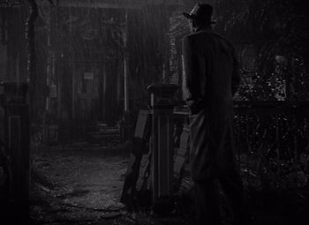 Movie still from “It's a Wonderful Life” (1946), directed by Frank Capra – A man standing in the rain next to an open door; Wide shot, Low angle