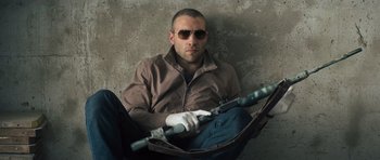 Movie still from “Jack Reacher” (2012), directed by Christopher McQuarrie – A man sitting on the ground holding a rifle; Medium shot, Low angle