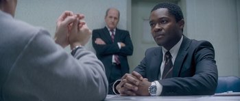 Movie still from “Jack Reacher” (2012), directed by Christopher McQuarrie – Three men in suits sitting at a conference table; Medium shot, Over the shoulder angle