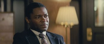 Movie still from “Jack Reacher” (2012), directed by Christopher McQuarrie – A man wearing a suit and tie in front of a lamp; Close Up shot, Over the shoulder angle