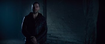 Movie still from “Jack Reacher” (2012), directed by Christopher McQuarrie – A man wearing a leather jacket standing next to a brick wall; Medium shot, Low angle