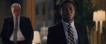 Movie still from “Jack Reacher” (2012), directed by Christopher McQuarrie – A man in a black suit and a tie; Close Up shot, Over the shoulder angle