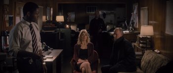 Movie still from “Jack Reacher” (2012), directed by Christopher McQuarrie – A woman sitting on a chair in a room with two other people; Wide shot, Over the shoulder angle