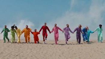 Movie still from “Jackass 4.5” (2022), directed by Jeff Tremaine – A group of people dressed in all different colors running on the beach; Wide shot, Low angle