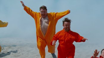 Movie still from “Jackass 4.5” (2022), directed by Jeff Tremaine – Two men in orange jumpsuits on the beach; Medium shot, Low angle