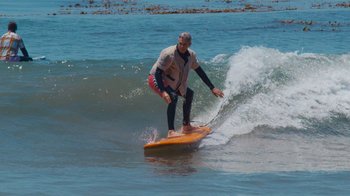 Movie still from “Jackass 4.5” (2022), directed by Jeff Tremaine – A man riding a wave on top of a surfboard in the ocean; Wide shot, Low angle