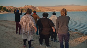 Movie still from “Jackass 4.5” (2022), directed by Jeff Tremaine – A group of people standing on a beach near a body of water; Wide shot, High angle