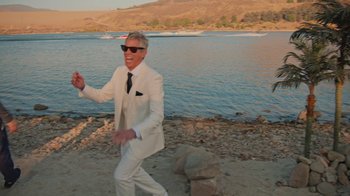 Movie still from “Jackass 4.5” (2022), directed by Jeff Tremaine – A man in a white suit is running on the beach; Medium shot, High angle