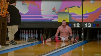 Movie still from “Jackass 4.5” (2022), directed by Jeff Tremaine – A man sitting on the floor of a bowling alley; Wide shot, Low angle